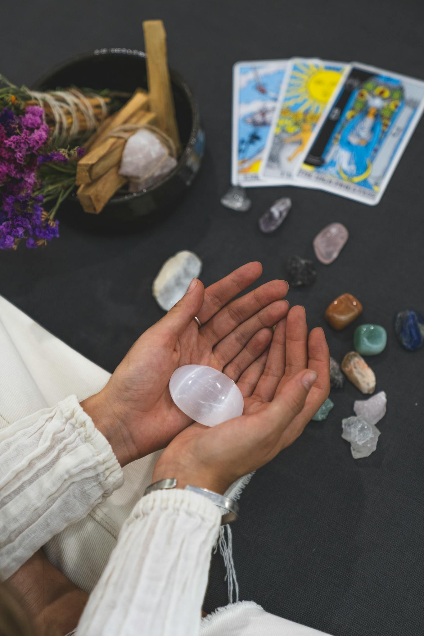 Close-up of hands holding healing stone with tarot cards on surface, promoting spiritual healing.